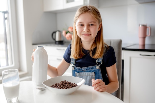 Süßes Mädchen sieht in den Rahmen, sitzend am Küchentisch mit trockenem Frühstück auf dem Teller