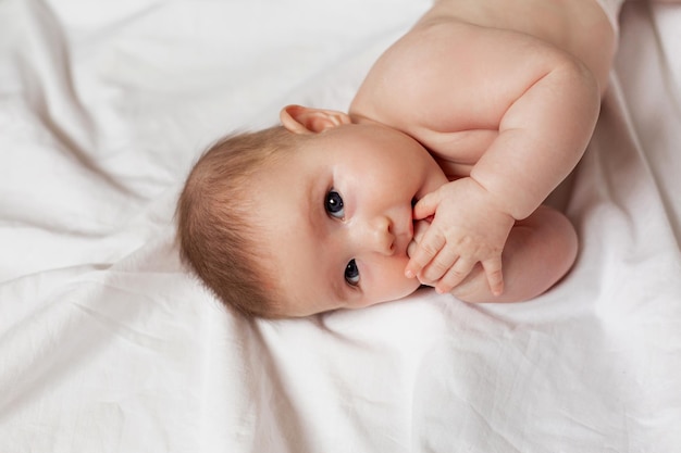 Süßes, nachdenkliches Neugeborenes liegt auf der Seite auf einem weißen Bett. Produkte für Kinder. konzept einer glücklichen kindheit und mutterschaft. Kinderbetreuung. Platz für Text. Foto in hoher Qualität