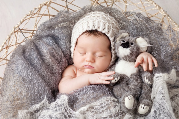 Süßes Neugeborenes Baby schläft in einem Korb. Schöner neugeborener Junge mit Bärenspielzeug.