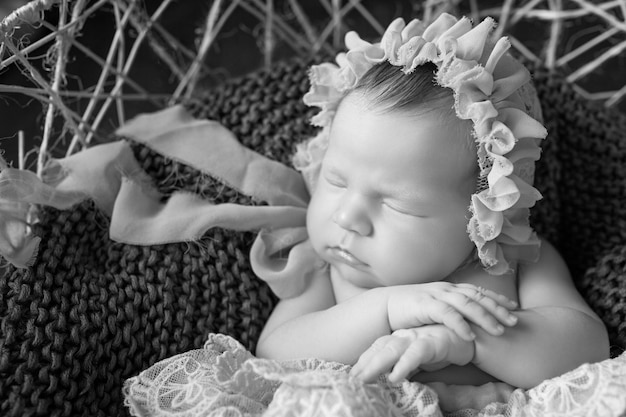 Süßes neugeborenes Baby schläft Neugeborenes Mädchen, 3 Wochen alt, liegt in einem Korb mit gestricktem Plaid Porträt eines hübschen neugeborenen Mädchens Nahaufnahmebild Dunkelbrauner Hintergrund