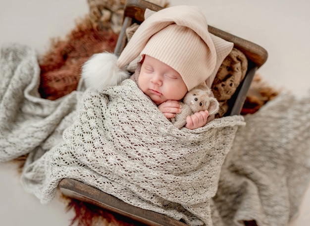 Süßes neugeborenes Baby schlafend im kleinen Bett, das beige Hut trägt