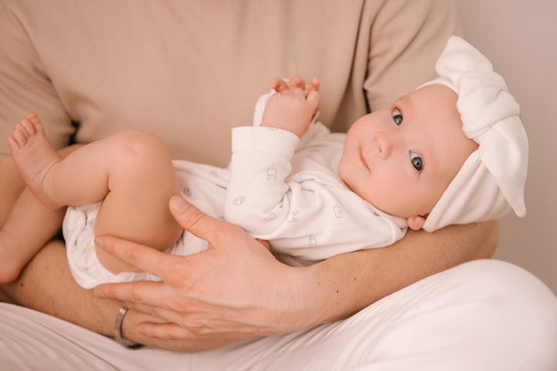 Süßes neugeborenes Mädchen in weißer Kleidung auf Papas Händen auf hellem Hintergrund