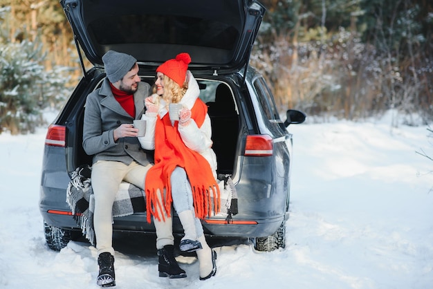 Süßes Paar, das Winterwald-Picknick hat und Tee aus Tee zum Mitnehmen Tasse Natur-Picknick-Liebesgeschichte-Date im Auto trinkt