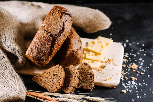 Süßes Roggenbrot und Weizen auf schwarzem Holzhintergrund