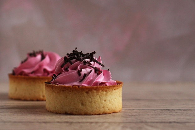 Süßes rundes Törtchen mit rosa Sahne und Schokolade auf rosa Hintergrund