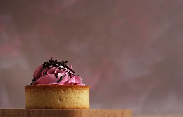 Süßes rundes Törtchen mit rosa Sahne und Schokolade auf rosa Hintergrund