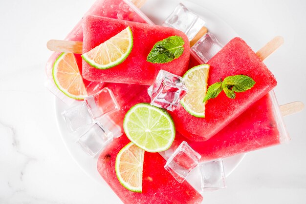 Süßes Sommerwassermelonen- und -kalkeis am stiel mit geschnittener Wassermelone und Minze