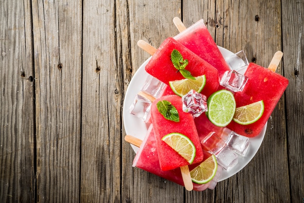 Süßes Sommerwassermelonen- und -kalkeis am stiel mit geschnittener Wassermelone und Minze