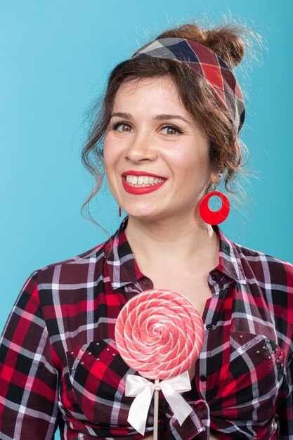 Süßigkeiten-, Diät- und Junk-Food-Konzept - Porträt der Pin-up-Frau mit großem Lutscher auf blauer Oberfläche