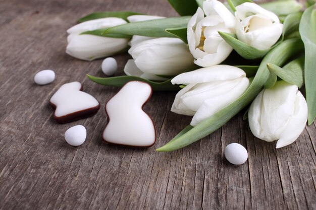 Süßigkeiten für Ostern. Weiße Tulpen, Schokoladeneier und Hase. Alter hölzerner Hintergrund.