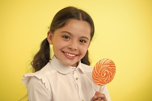 Süßigkeiten-Lollipop Lieblings-Leckereien der Schüler Spaß mit Süßigkeiten Mädchen Kind Pferdeschwänze Frisur essen süßes Lollipop Mädchen Schüler Schuluniform wie süßes Lollipop gelber Hintergrund Ihr Lieblingsgeschmack