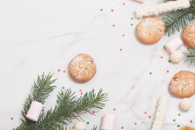 Süßigkeiten und Kekse mit Weihnachtsbaumzweigen auf weißem Marmorhintergrund