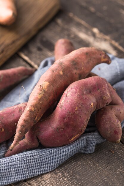 Süßkartoffel auf Holzbrett Hintergrund, Nahaufnahme. Rohe Süßkartoffeln oder Batatas mit Kräutern