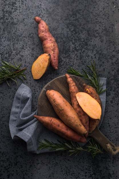 Süßkartoffel auf Holzbrett Hintergrund, Nahaufnahme. Rohe Süßkartoffeln oder Batatas mit Kräutern