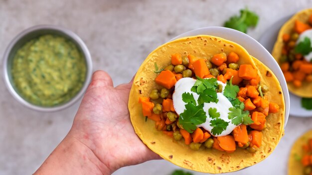 Süßkartoffel-Chickpeas-Tacos mit Coriander-Crema auf einem handgehaltenen Teller Generative KI