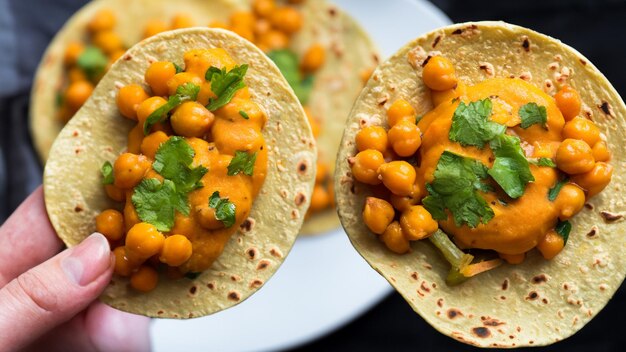 Süßkartoffel-Chickpeas-Tacos mit Coriander-Crema auf einem handgehaltenen Teller Generative KI