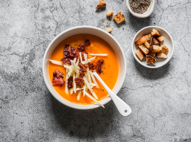 Süßkartoffelpüreesuppe mit knusprigen Speckcroutons und Apfel auf einer Draufsicht des grauen Hintergrundes