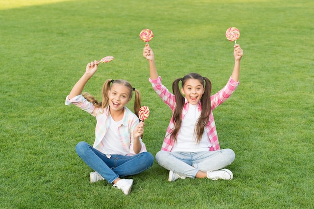 Süßwaren Süßes Karamell Glückliche Kinder halten Süßigkeiten sitzen Gras Süßigkeitenladen Lollipop behandelt Süßigkeiten bedeutet Glück Zucker und Kalorien Fröhliche, fröhliche Freunde, die im Freien Süßigkeiten essen