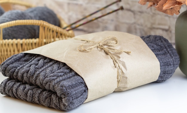 Suéter cinza feito à mão embalado em papel kraft. camisola de malha feita à mão. no fundo, uma cesta de vime com agulhas de tricô.