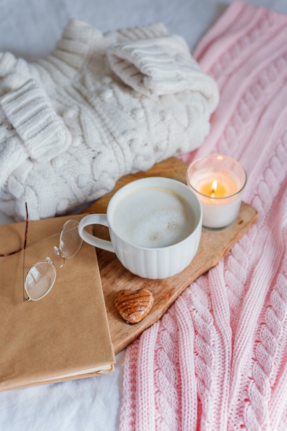 Suéter de malha, xadrez rosa, vela, caneca de cappuccino, livro, óculos na cama. café da manhã aconchegante. inverno. outono.