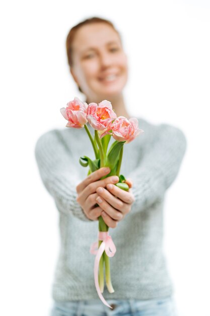 Suéter gris de mujer hermosa joven da tulipanes rosas sobre fondo blanco. Desenfoque de retrato, enfoque selectivo. 8 de marzo y día de la madre.