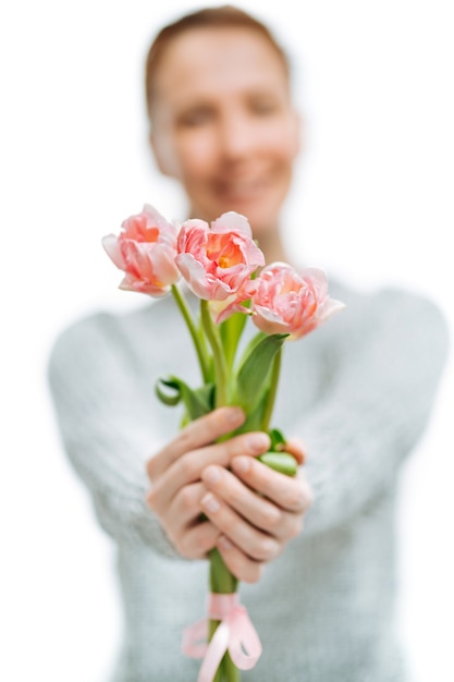 Suéter gris de mujer hermosa joven da tulipanes rosas sobre fondo blanco. Desenfoque de retrato, enfoque selectivo.