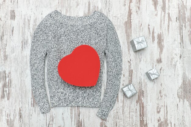 Suéter de punto gris, en forma de corazón rojo y cajas de regalo plateadas. Concepto de moda