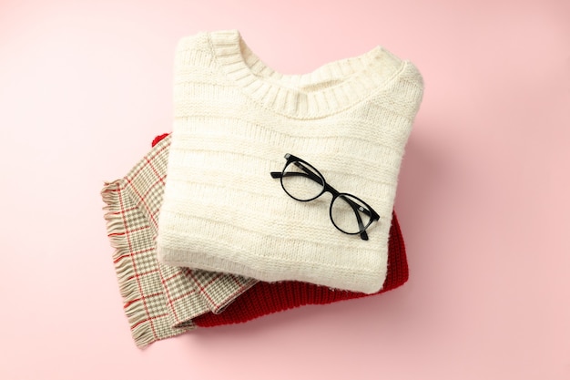 Suéteres e cachecol com óculos no fundo rosa.