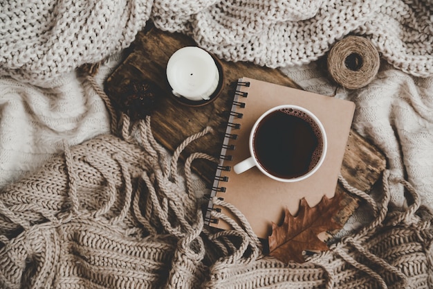 Suéteres y taza de té con cuaderno, velas y ropa de tejer