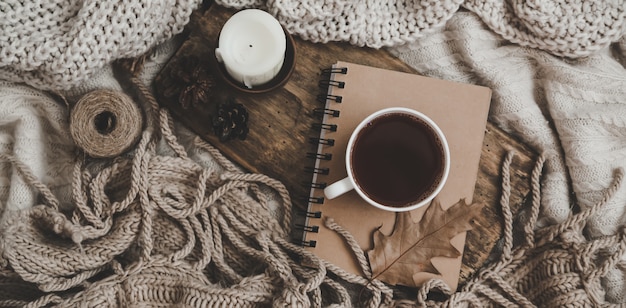Suéteres y taza de té con cuaderno, velas y ropa de tejer