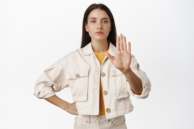 Suficiente, mantén la distancia. Chica seria extiende la mano en tabú, señal de pare, di no a algo malo, prohíbe o restringe algo, rechaza la oferta, de pie en blanco