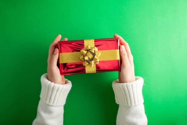 Sumérgete en la magia de las fiestas Vista superior en primera persona de las manos alcanza la lujosa caja de regalos roja con lazo de cinta en fondo verde Perfecto para el marketing del día de San Valentín