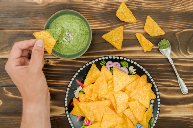 Foto sumergir a mano los nachos en guacamole.