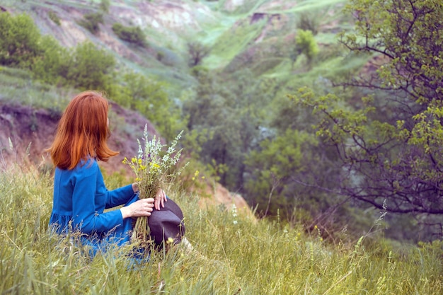 Summer - linda garota em um prado com um buquê de flores silvestres e uma paisagem tradicional ucraniana