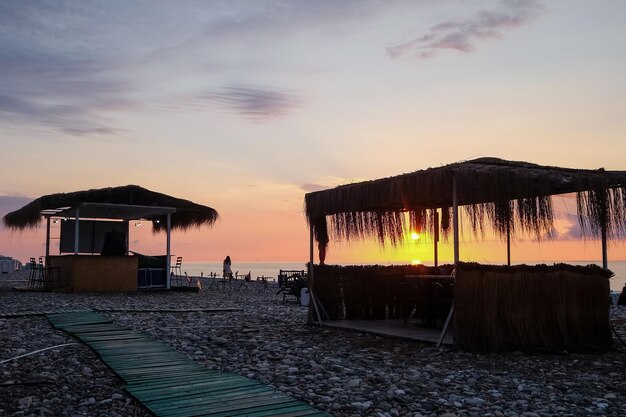 Sunset um gazebo com um telhado de junco na costa do mar.