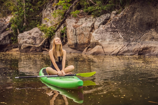 SUP Stand Up Paddle Board Frau Paddle Boarding auf See stehend glücklich auf Paddleboard auf blauem Wasser Action Shot of Young Woman on Paddle Board