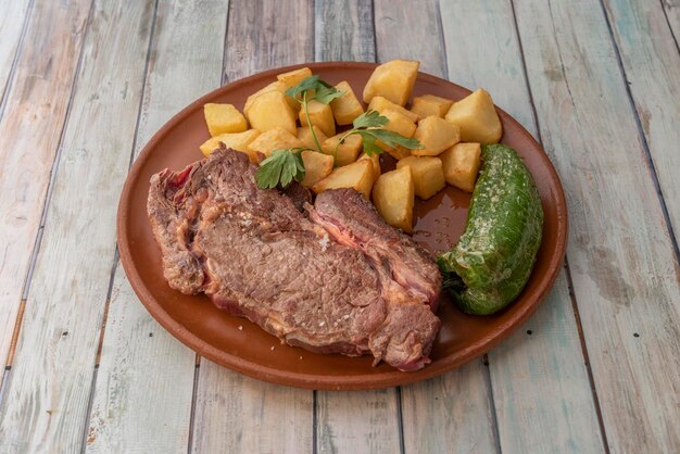 Foto súper entrecot de ternera a la brasa con pimiento verde frito y guarnición de dados de patata frita a la sal marina