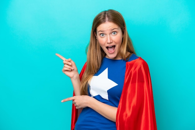 Foto super hero kaukasische frau isoliert auf blauem hintergrund überrascht und zeigt seite