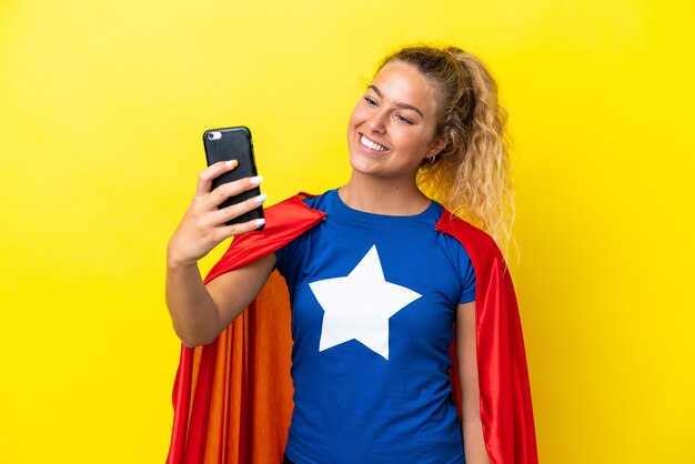 Super Hero mujer aislada sobre fondo amarillo haciendo un selfie con teléfono móvil