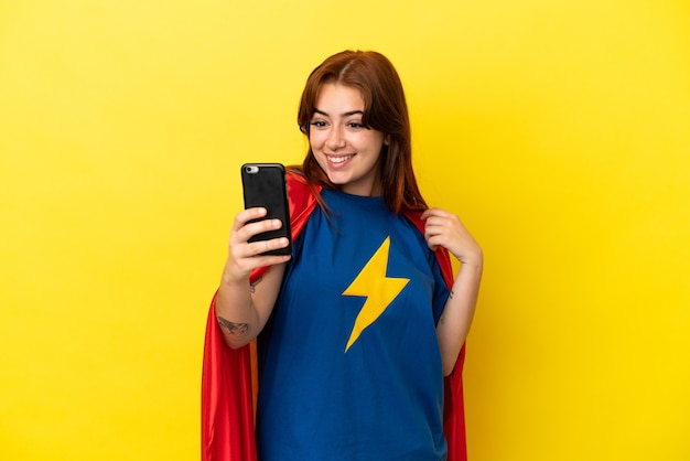 Super Hero Rothaarige Frau isoliert auf gelbem Hintergrund macht ein Selfie