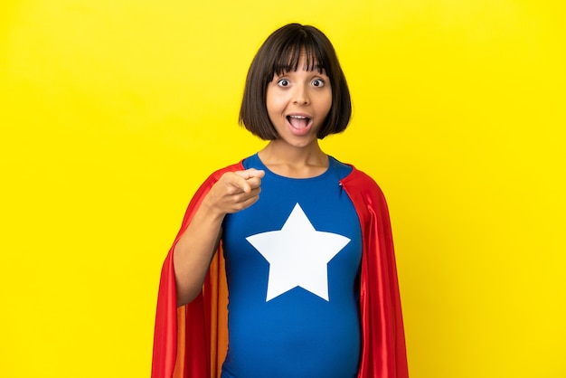 Foto super hero schwangere frau isoliert auf gelbem hintergrund überrascht und zeigt nach vorne