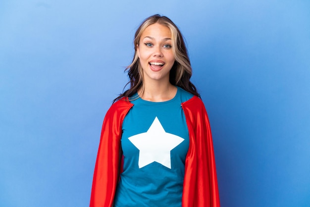 Super Hero Teenager Mädchen auf blauem Hintergrund mit Überraschungsgesichtsausdruck isoliert