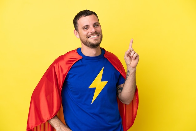 Foto super herói brasileiro homem isolado em fundo amarelo mostrando e levantando dedo em sinal dos melhores