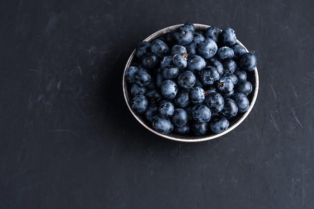 Superalimento orgánico antioxidante de arándanos en un tazón de cerámica para una alimentación saludable y una nutrición dietética Vista superior en negro oscuro