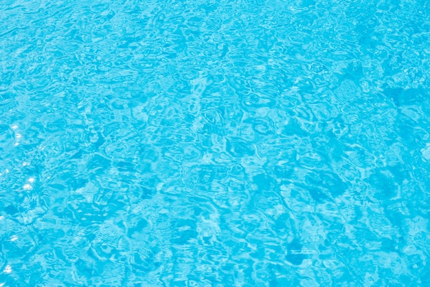 Superficie del agua azul de la piscina con el reflejo de luz del sol brillante.