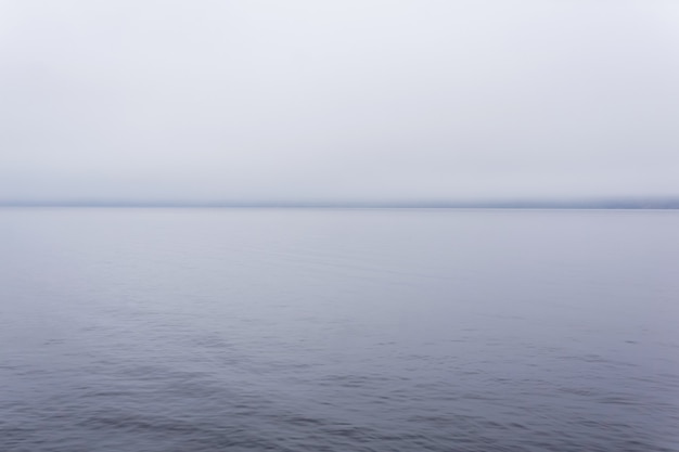 Superficie de agua fría en la niebla con una costa distante apenas visible en el horizonte