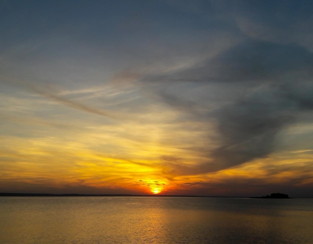 Superficie del agua del mar al atardecer con un sol brillante sobre el horizonte y una isla distante a la derecha