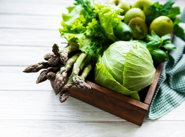 Superficie de concepto de comida vegetariana saludable, selección de alimentos verdes frescos para la dieta de desintoxicación, caja con manzana, pepino, espárragos, aguacate, lima, vista superior de ensalada sobre una superficie de madera blanca