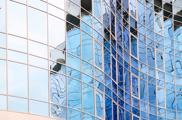 Superficie de cristal del espejo del rascacielos que refleja el cielo nublado, superficie con curvas