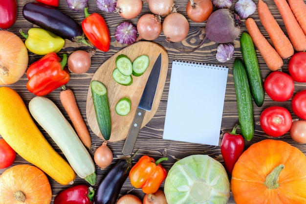 Superficie de cuaderno y verduras frescas en mesa de madera. Concepto de alimentos crudos.